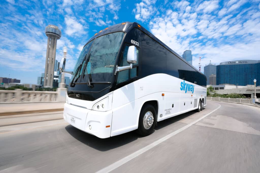 Skyway Charters bus turning on a downtown Dallas street with Reunion Tower and Omni Hotel in the background